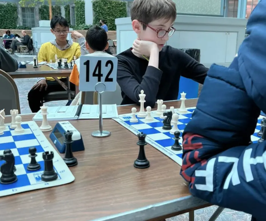 A young player seated behind a board marker reading 142, chin in hand, studying the position.